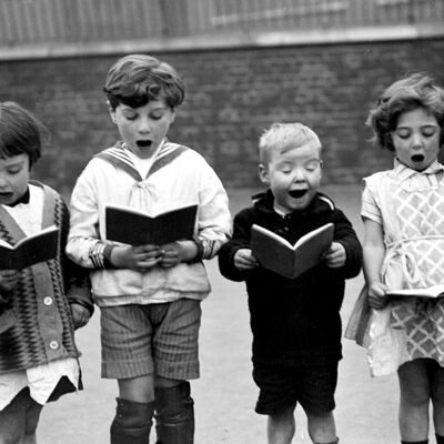 Niños cantando en la tarjeta de saludos en blanco del patio de la escuela
