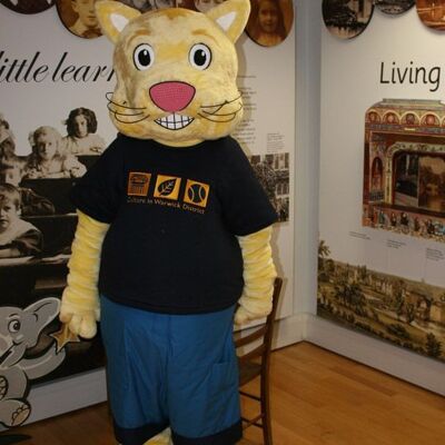 Costume de mascotte personnalisable de chat jaune en tenue bleue et noire.