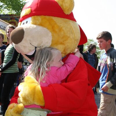 Costume de mascotte personnalisable de gros ours jaune et rouge avec une casquette.