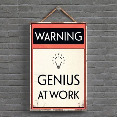 P1591 - Señal tipográfica de advertencia Genius At Work impresa en una placa colgante de madera
