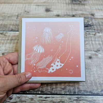 Swimming with Jellyfish - Blank greeting card in coral pink featuring a woman swimming underwater amongst Jellyfish