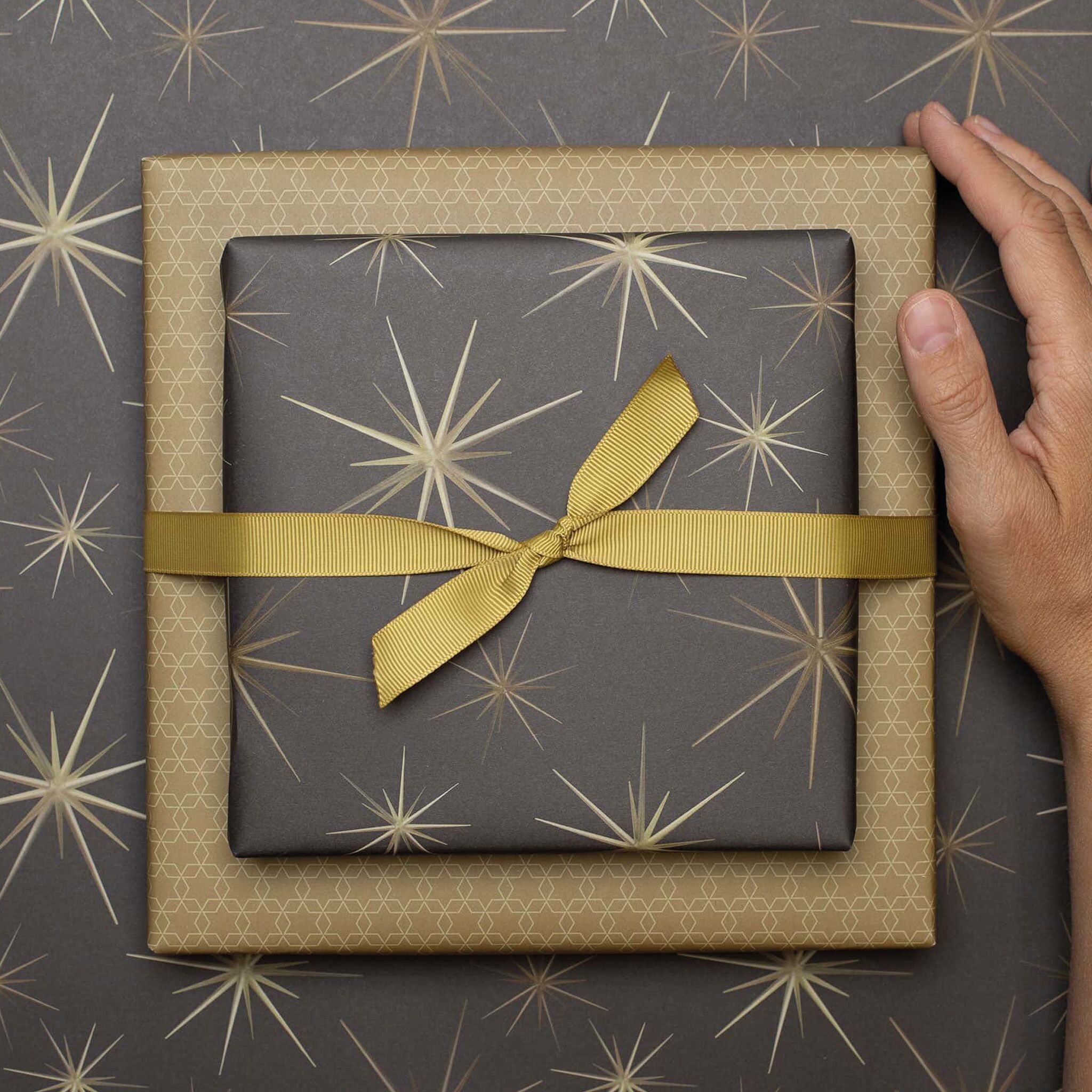 Geschenkpapier "Starburst" mit goldgelben Sternornamenten vor braunem Hintergrund - doppelseitig bedruckt auf 100% Recyclingpapier