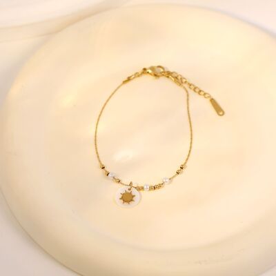 Goldenes Perlenarmband und goldene Perlen mit Sonnenanhänger auf Perlmutt