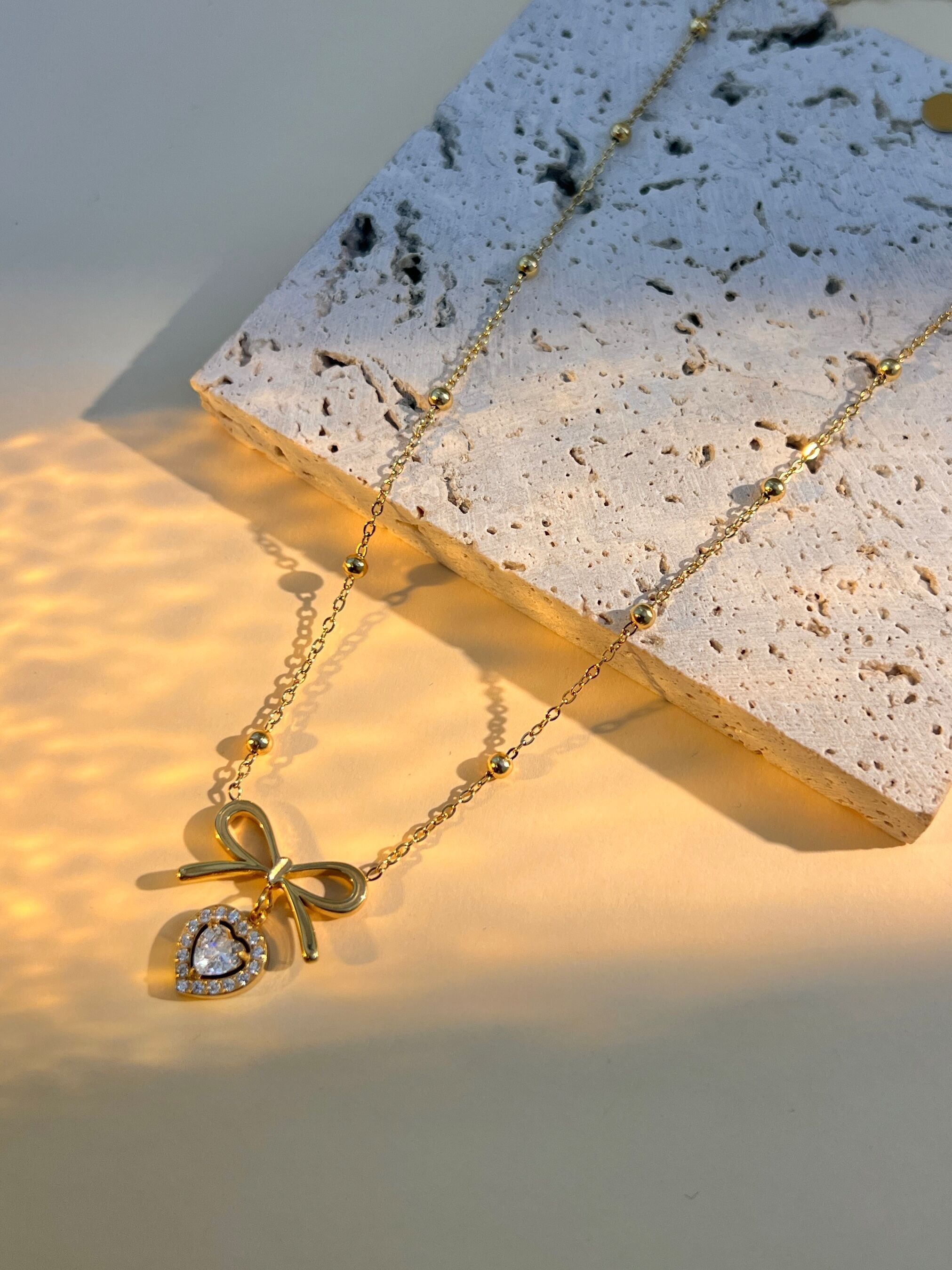 Collar de acero inoxidable con colgante de lazo y pequeño corazón de cristal.