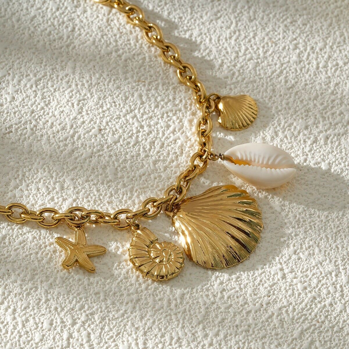 Collana a catena in oro con ciondoli a forma di conchiglia, ciprea bianca e stella marina