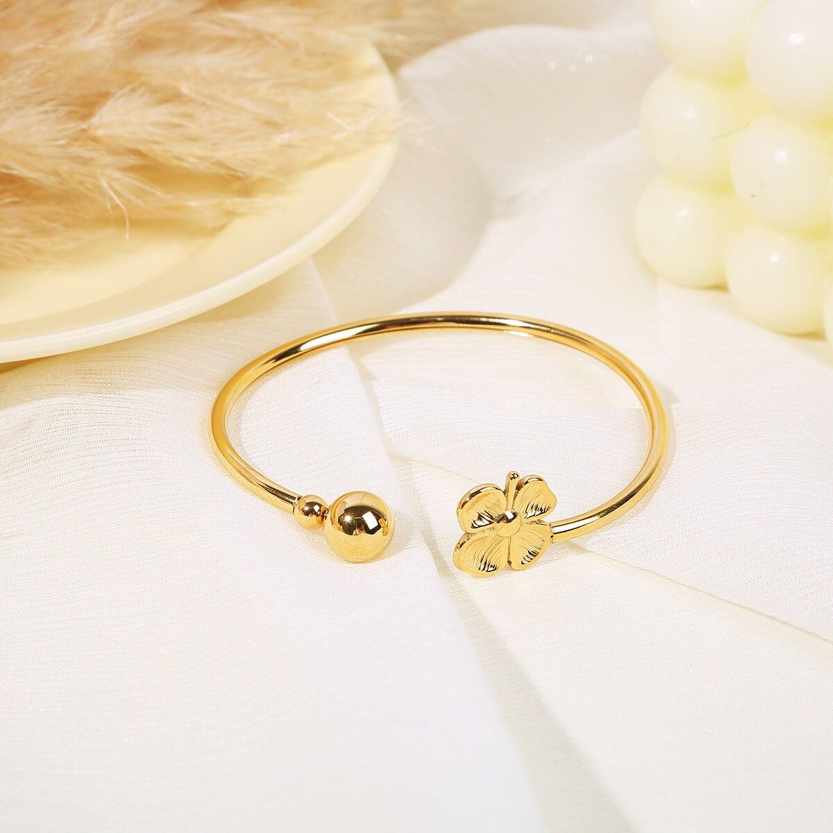 Goldener Armreif mit Öffnung vorne und einer goldenen Perle und einem vierblättrigen Kleeblatt an den Enden