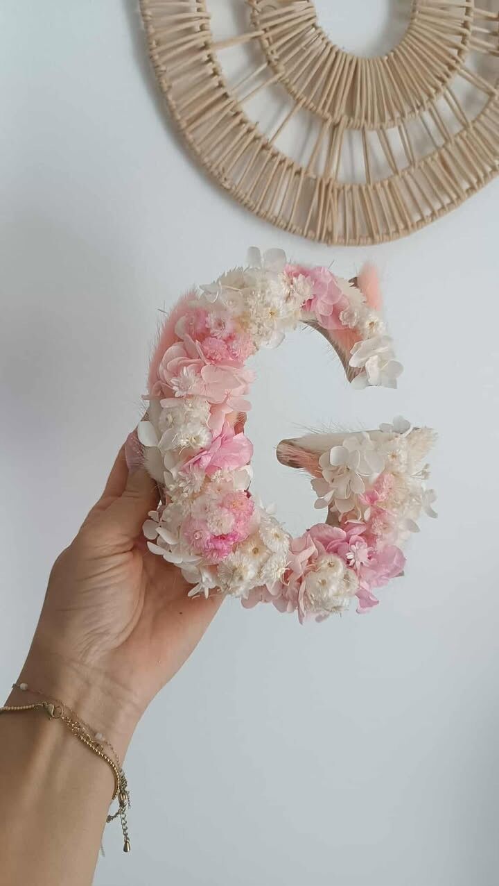 Letra floral en rosa pastel y flores secas blancas.