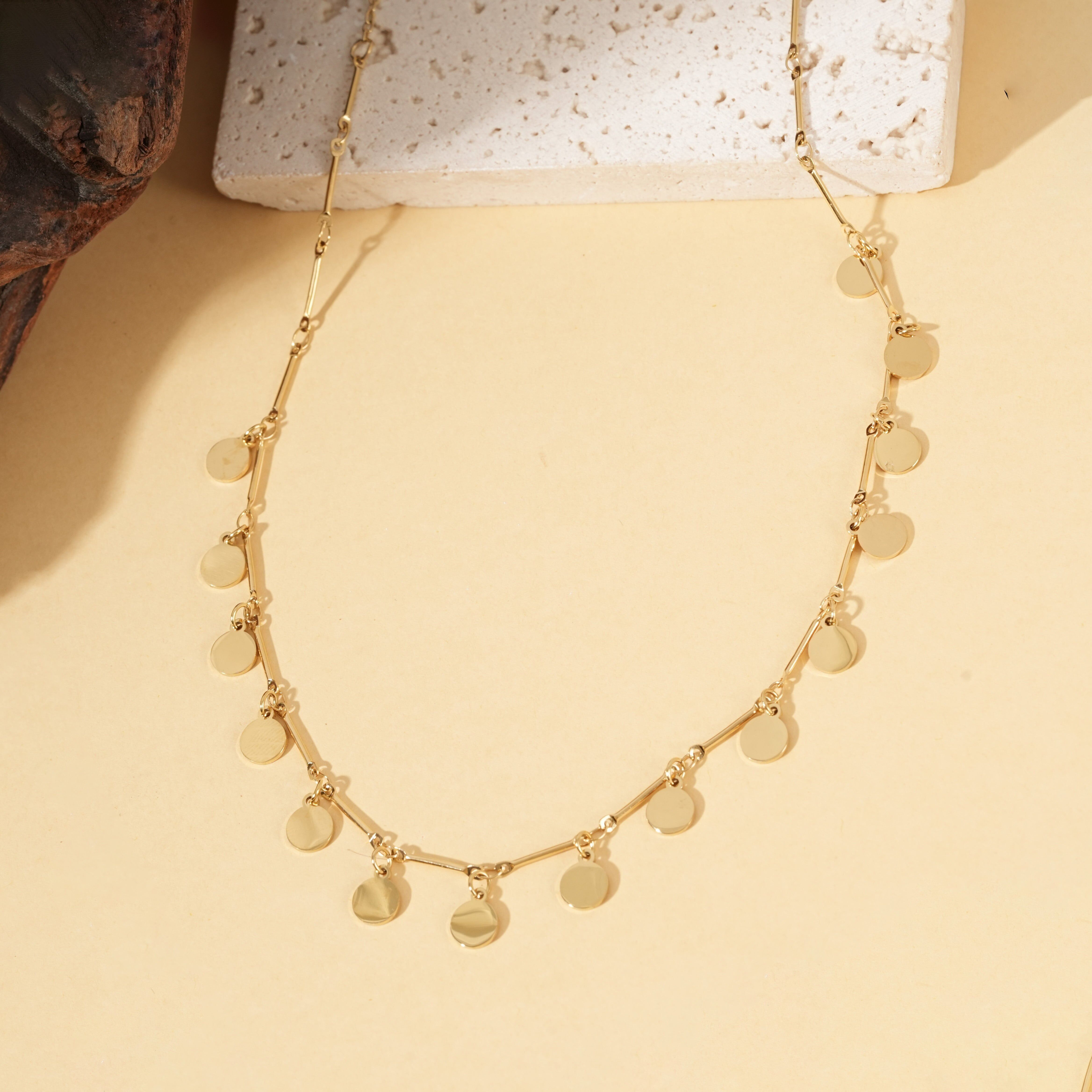 Collana color oro con una catena sottile ornata da dischi rotondi lucidi e barre lisce