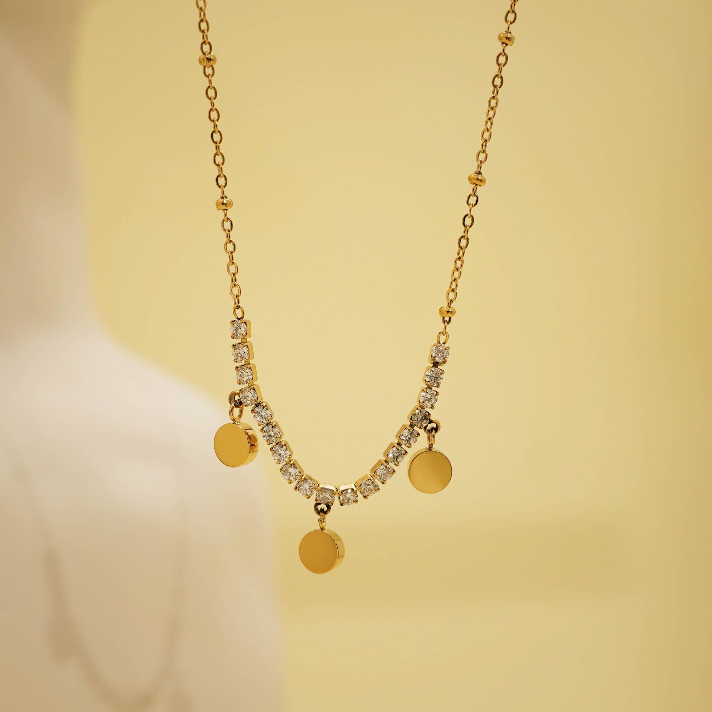 Collana color oro con catena sottile, una fila di strass e 3 nappe lisce e rotonde.