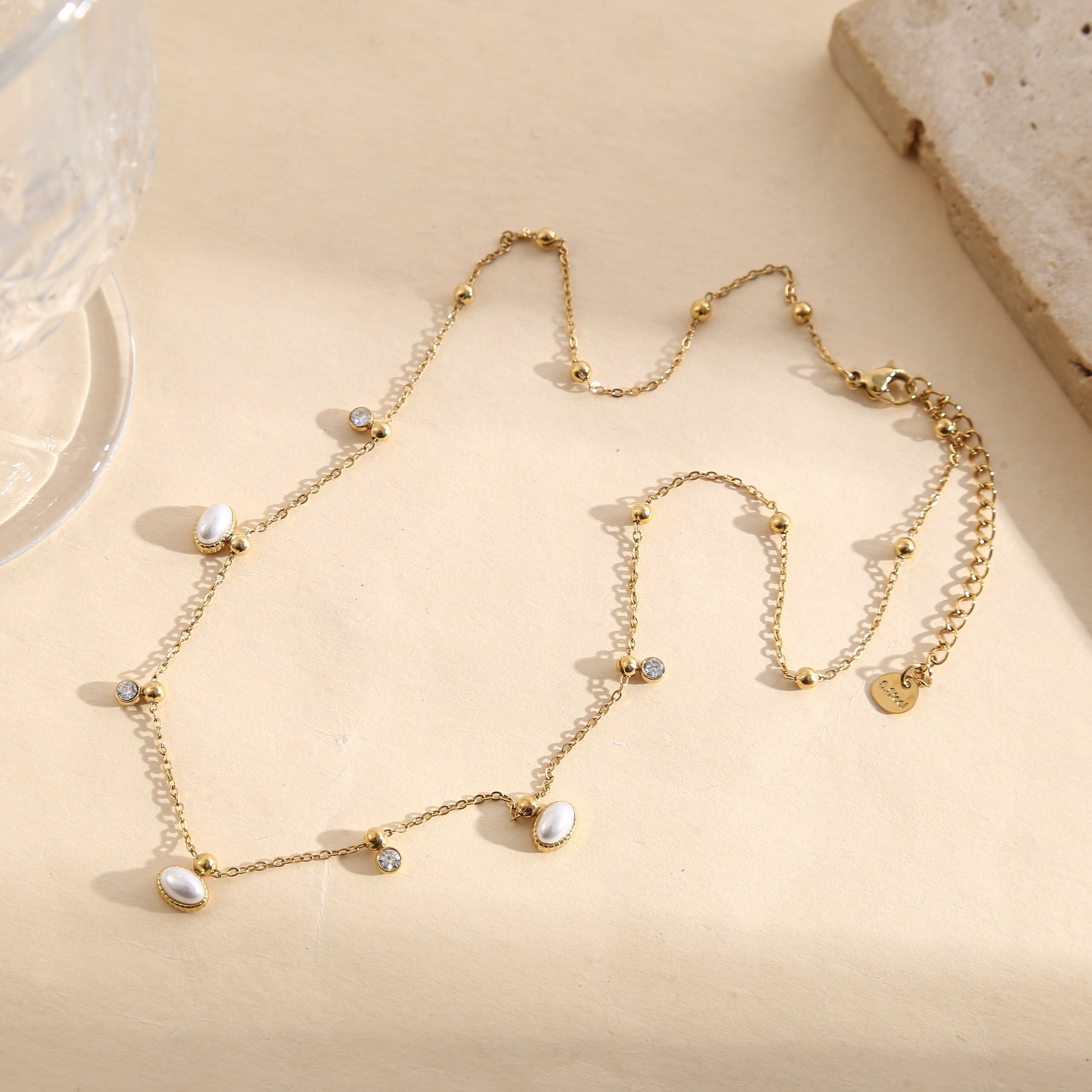 Collana in oro con catena sottile, perline dorate lisce e mini pendenti con strass.