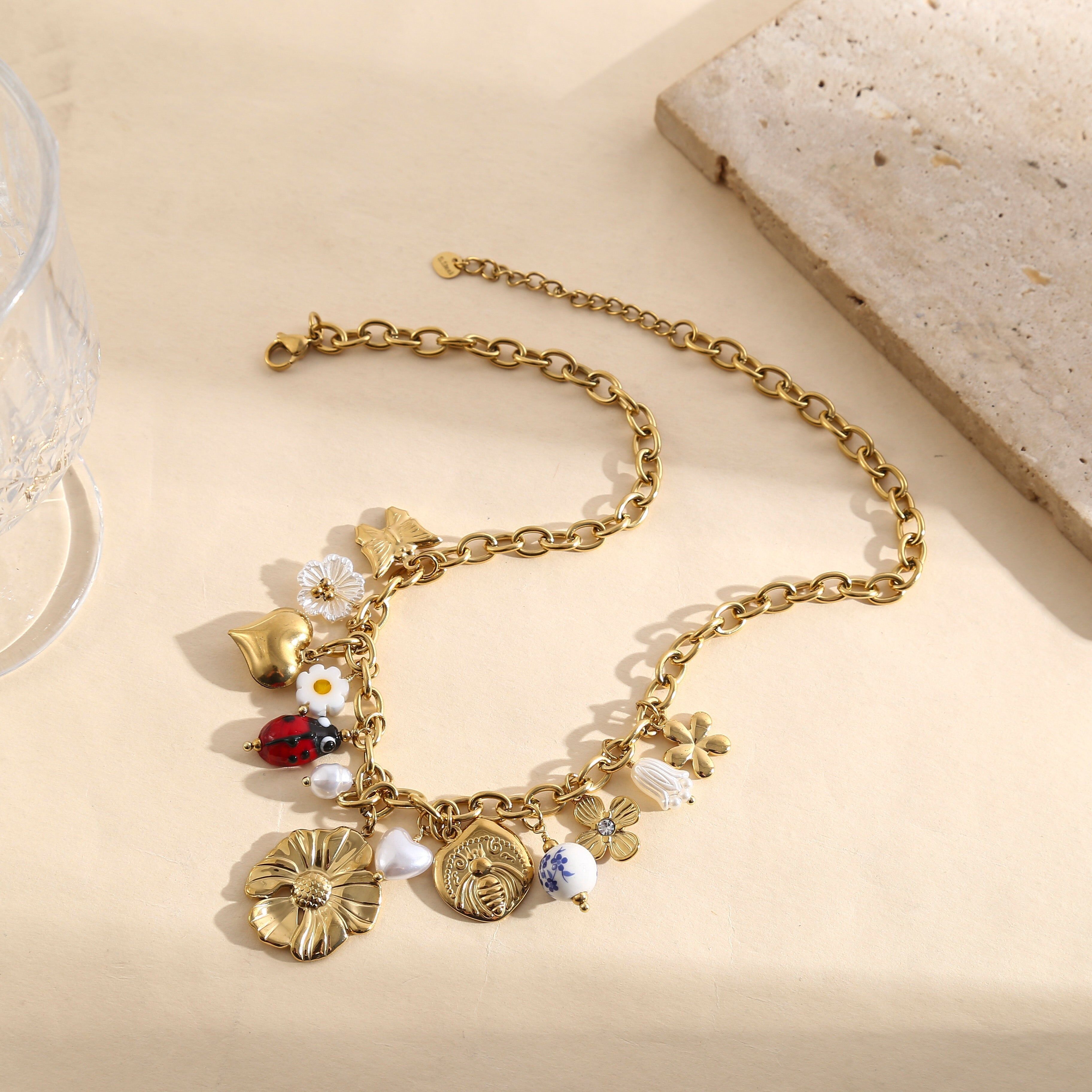 Collana a catena in oro con nappe floreali, ciondoli a forma di cuore, coccinella smaltata e medaglione inciso