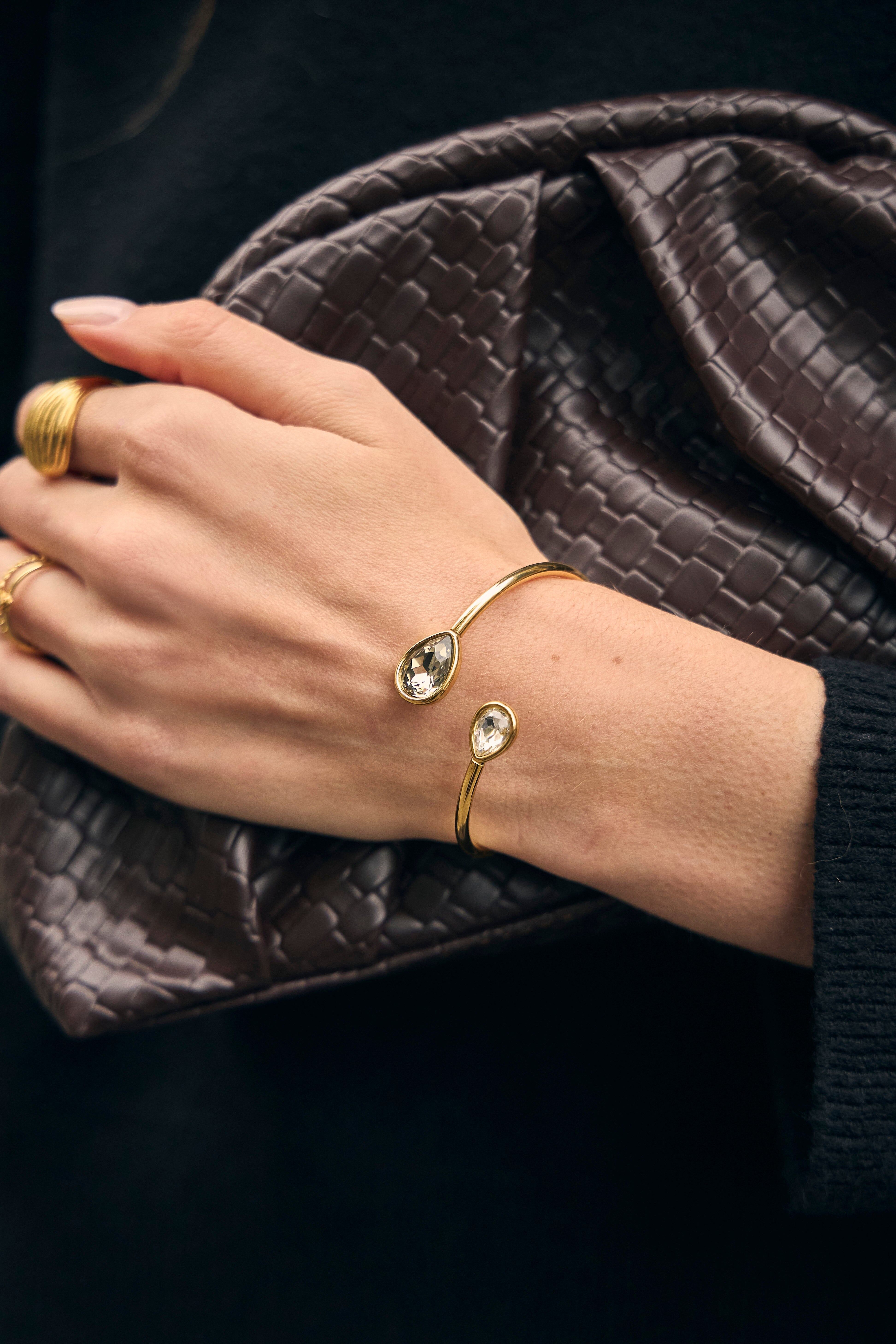 Bracciale rigido staccabile color oro, aperto sul davanti, con cristalli di vetro a goccia bianchi e grigi