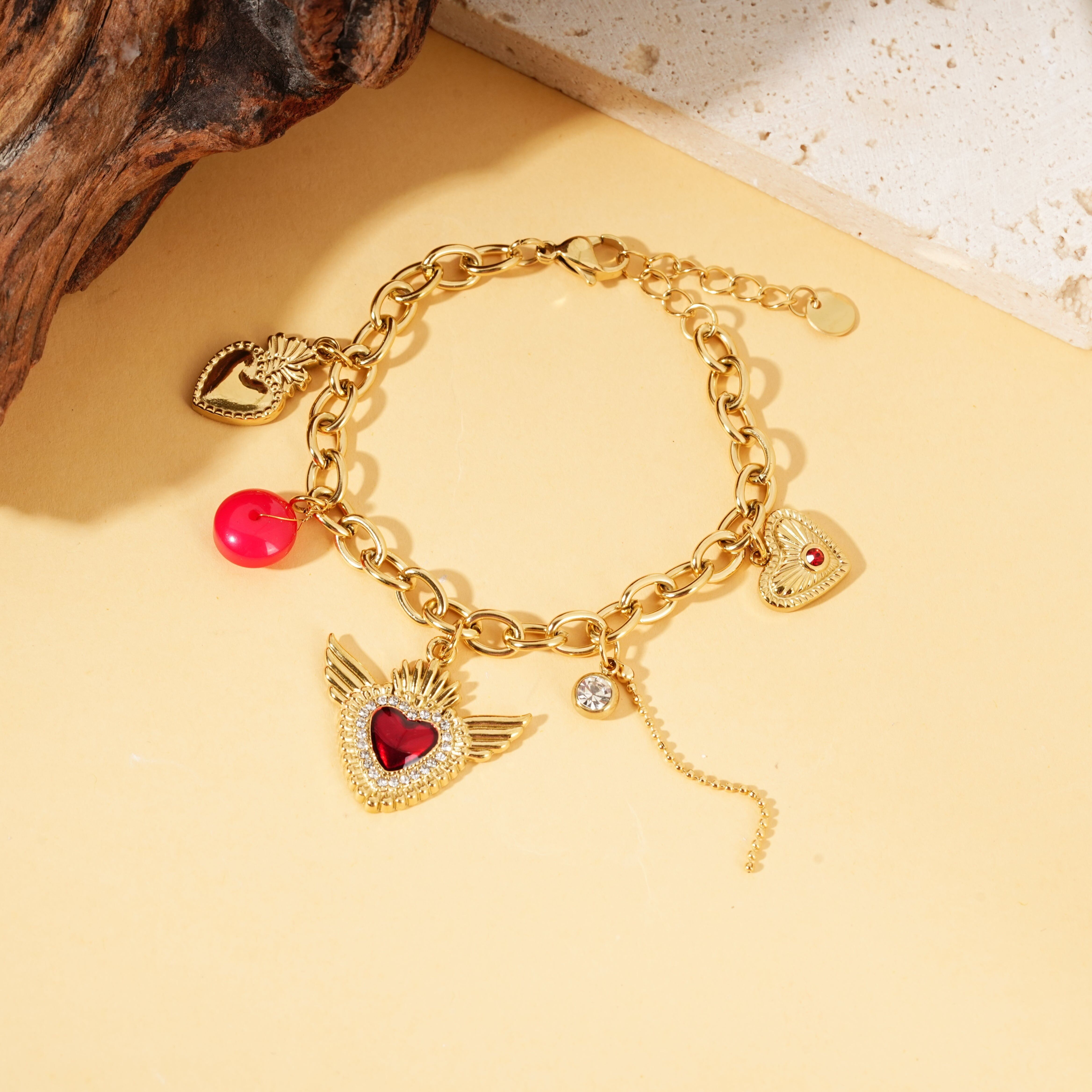 Bracciale in oro con ciondoli a forma di cuore, ali ex voto e strass rossi