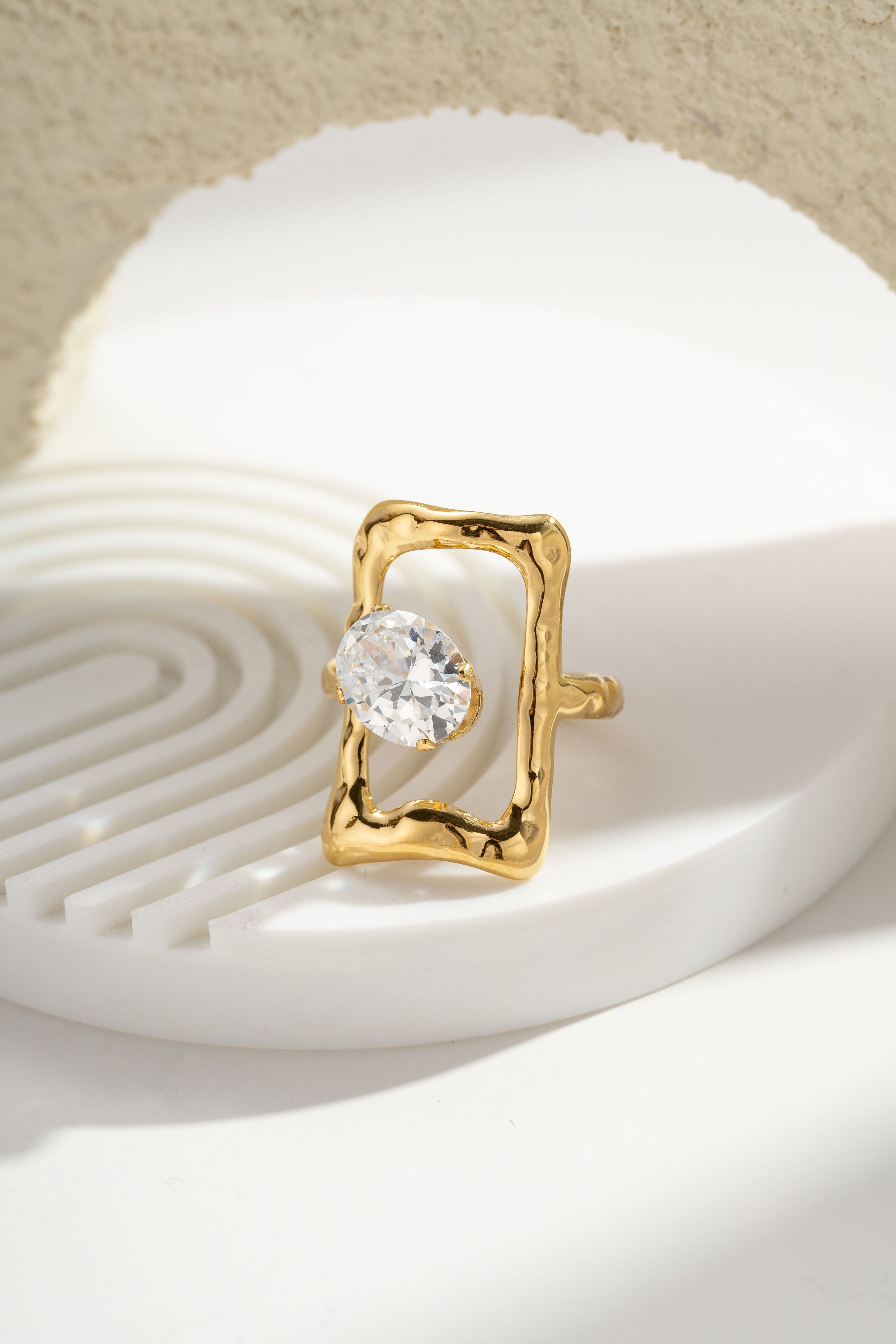 Goldring mit klarem, ovalem Stein und strukturiertem Stahlrahmen