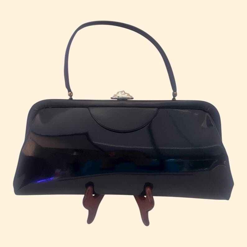 Schwarze Lacklederhandtasche aus den 1960er Jahren mit goldenem ovalem Akzent – ein Vintage-Stil der Mid-Century-Ära.