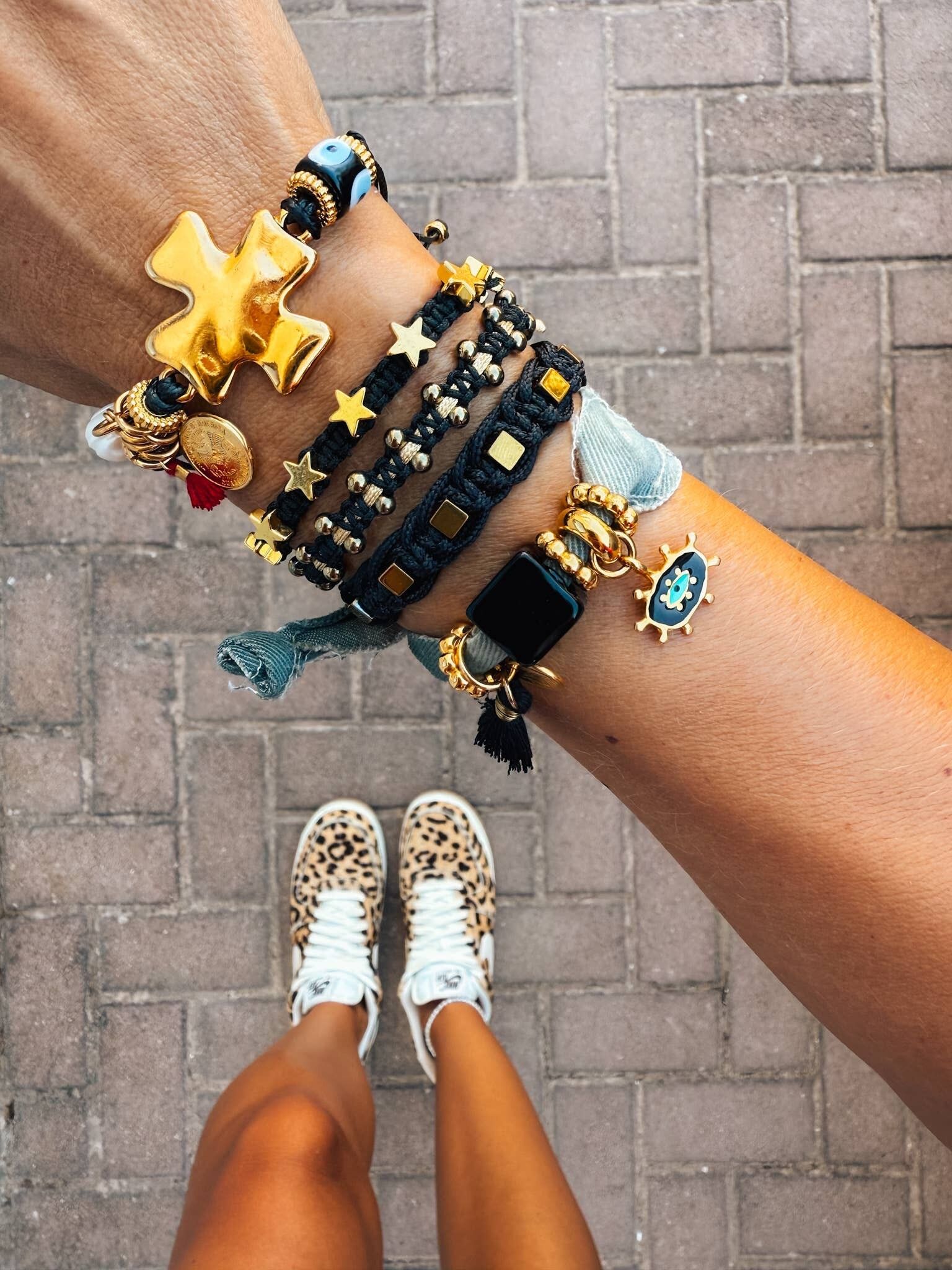 Pulsera apilada de oro y negro con cruz y estrellas