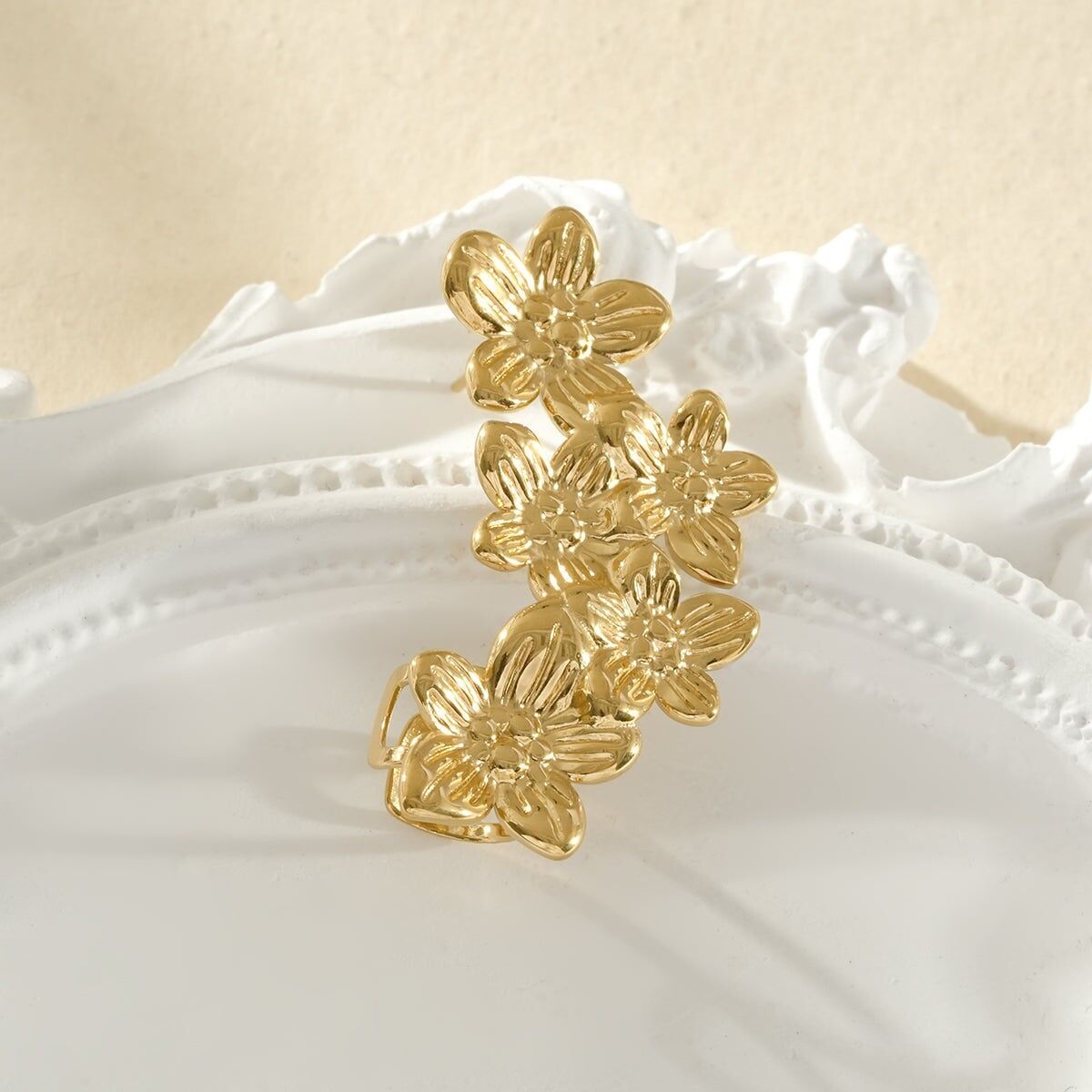 Gold ear cuff with five five-petaled flowers of varying sizes on the right side