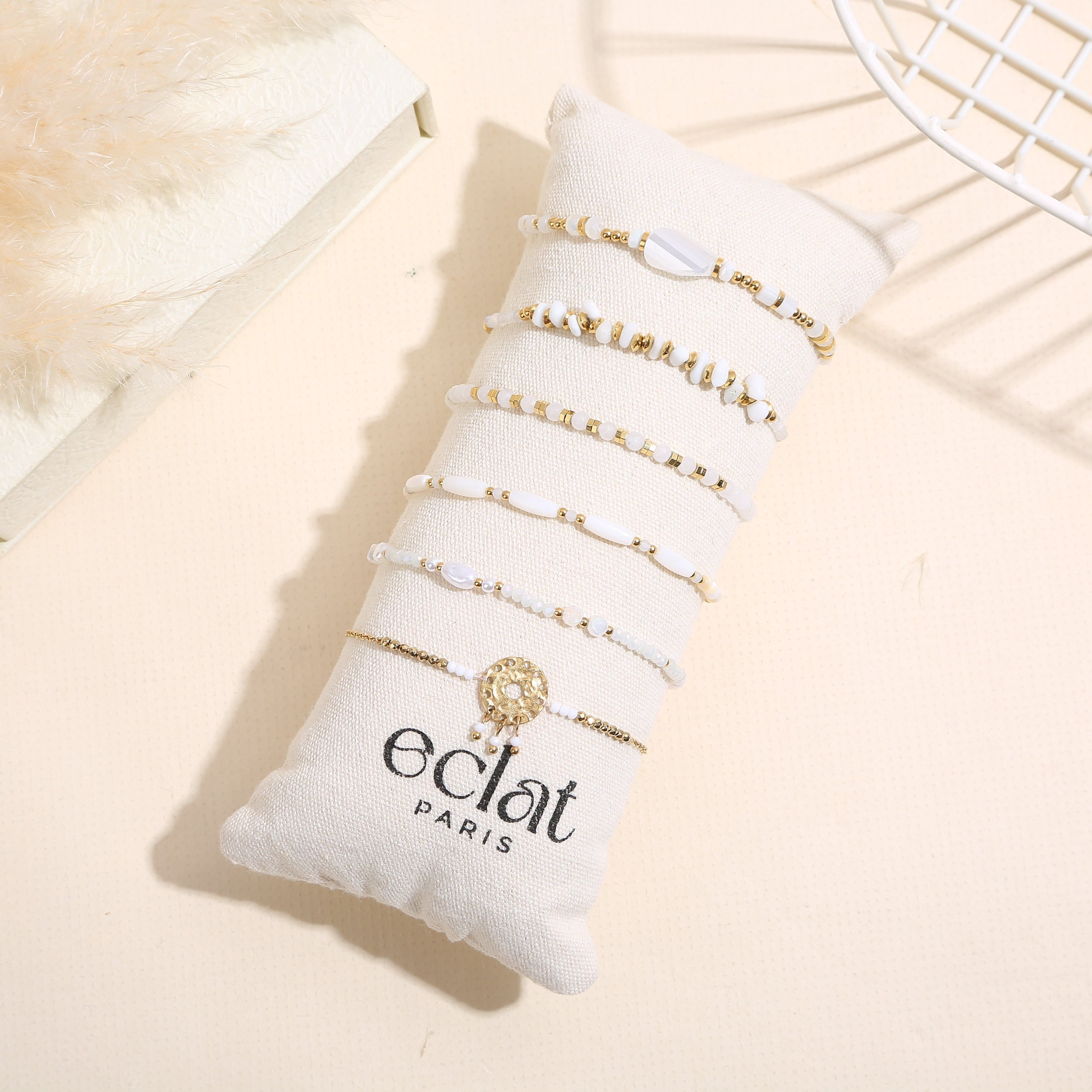 Set aus 6 goldenen Armbändern in Weißtönen auf einem Kissen