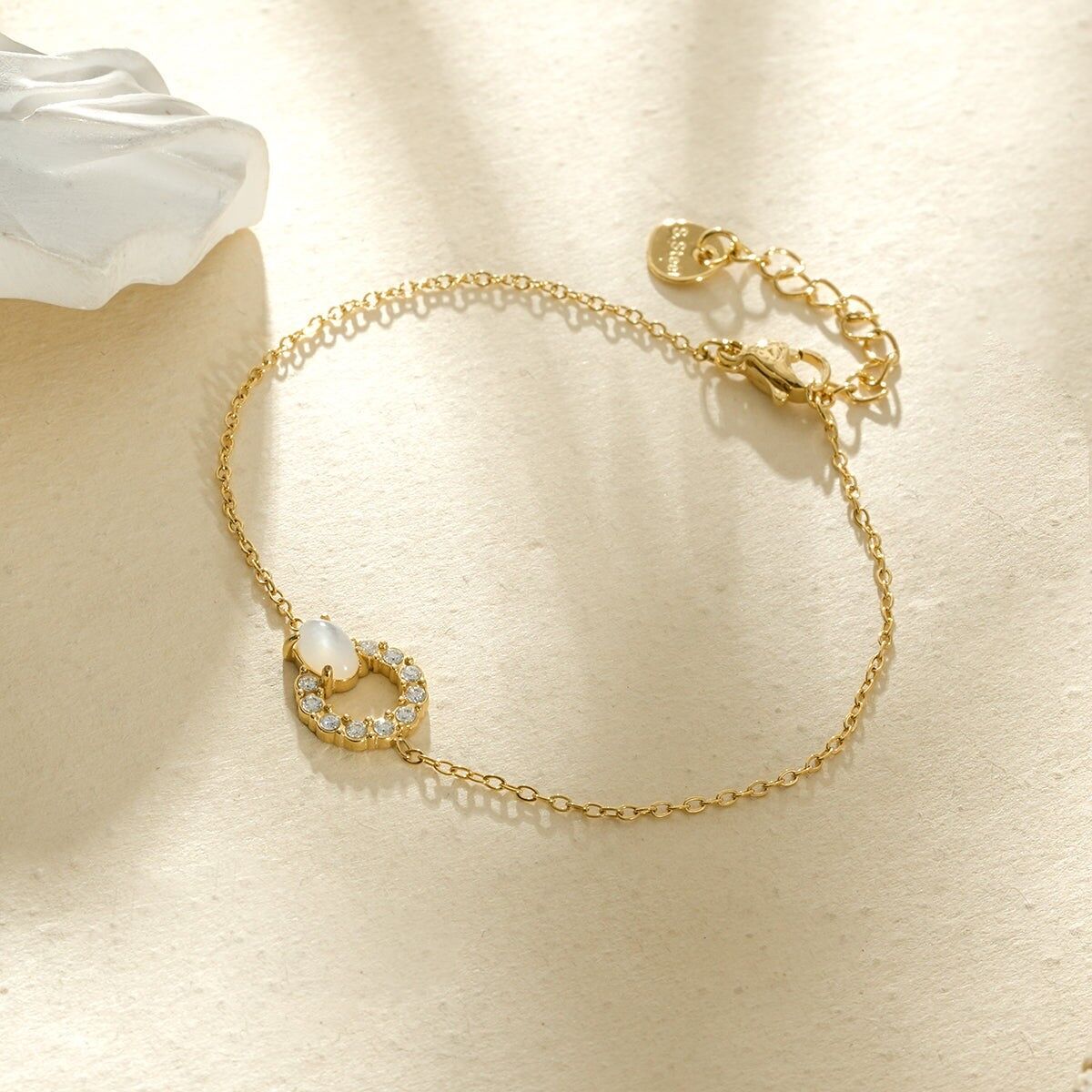 Goldfarbenes Armband mit feiner Kette, verziert mit einem kreisförmigen, mit Strasssteinen pavébesetzten Ring und einem perlmuttweißen Cabochon