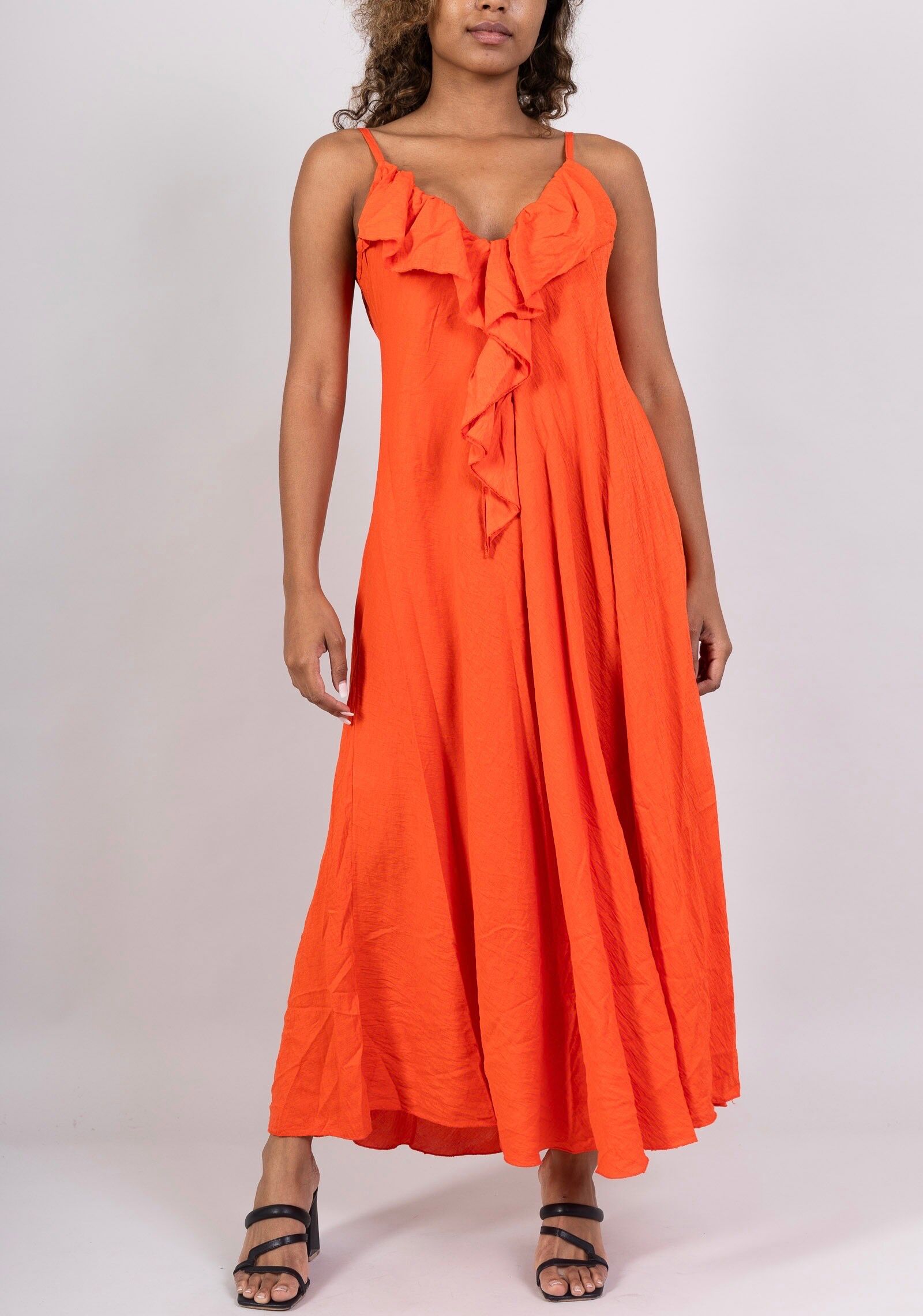 Long dress with thin straps and a plunging V-neck, highlighted by an elegant asymmetrical ruffle at the front.