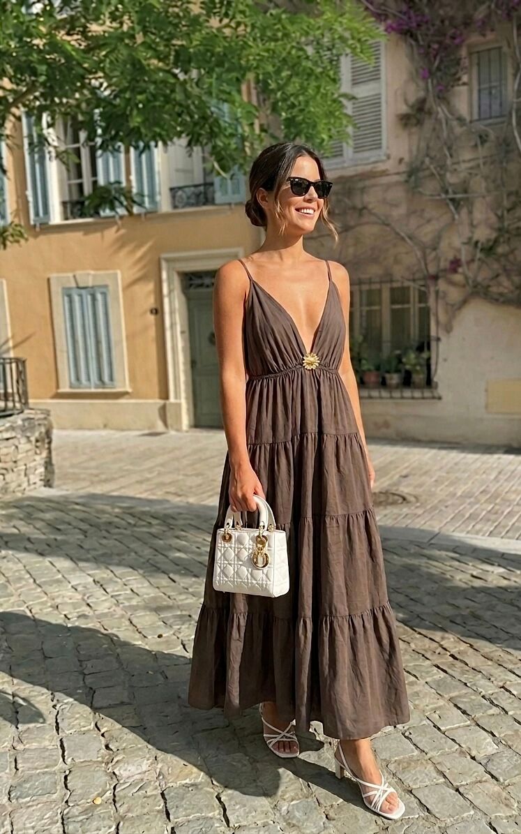 Flowy bohemian maxi dress with tiered empire waist, gathered under the bust, deep V-neck, thin adjustable straps, decorative gold flower embellishment, and two side pockets.