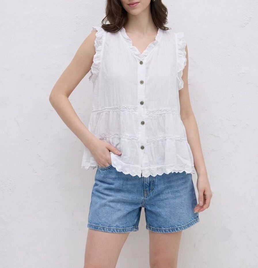 Sleeveless flared shirt with a V-neck, openwork lace trim, ruffles at the armholes and along the neckline, and a scalloped hem.