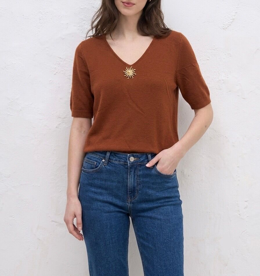 Fine knit sweater with short sleeves and ribbed trim, gold sun brooch affixed to the hollow of the neckline