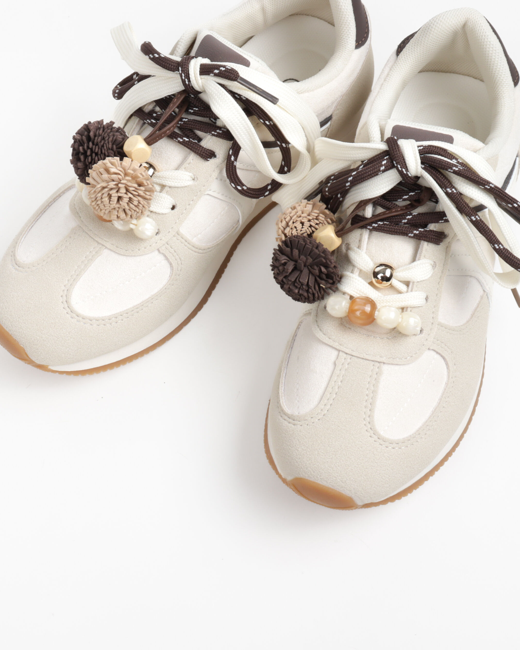 Women's low-top sneakers with a suede-like finish, contrasting laces, and pom-pom details.